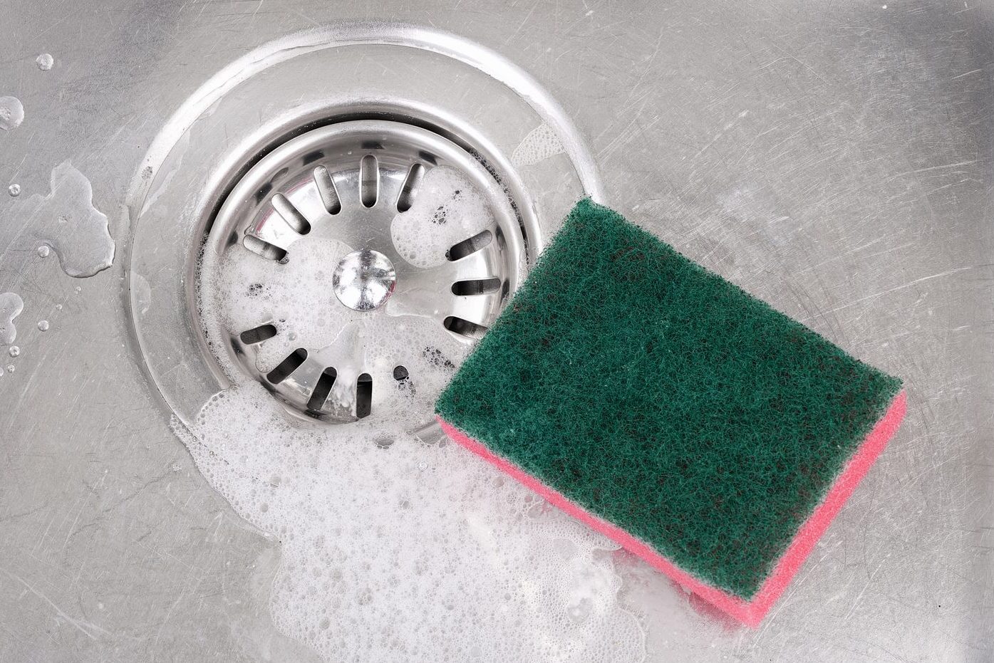 Stainless steel kitchen sink with soap suds and cleaning sponge