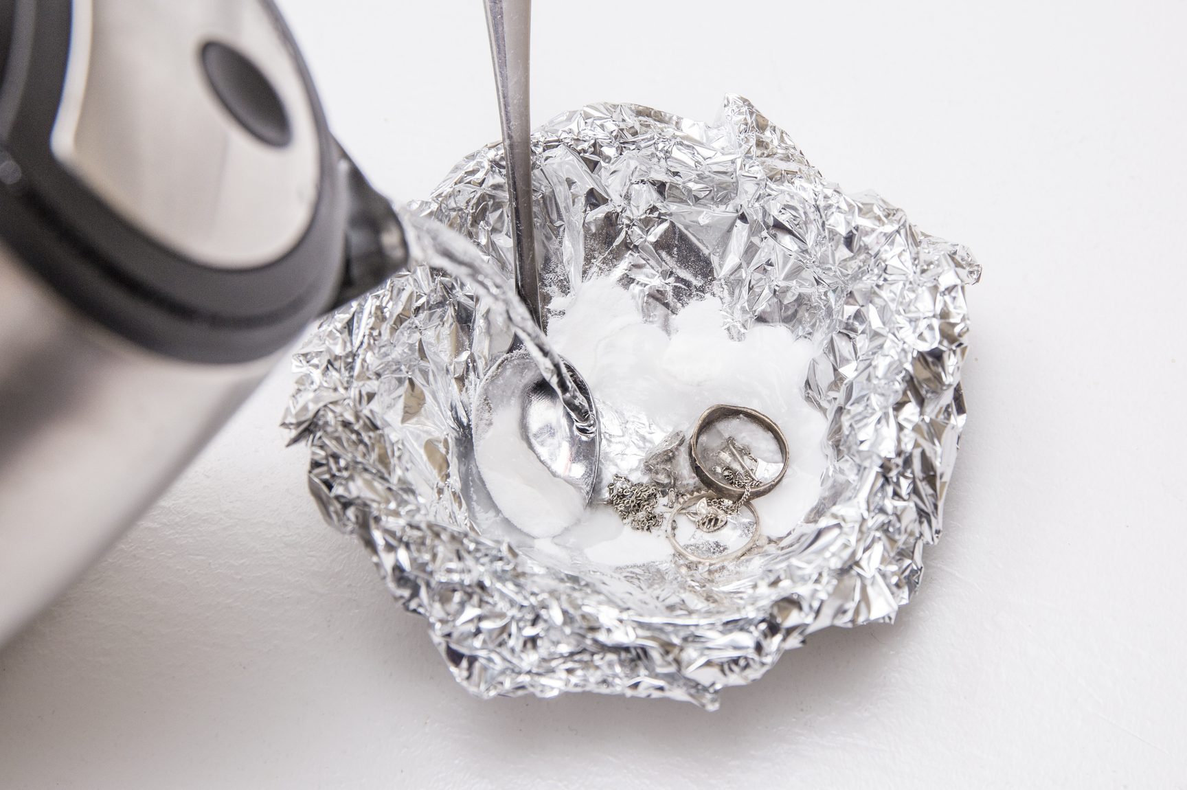 A solution of baking soda(Sodium bicarbonate) and warm water will remove the tarnish from silver when the silver is in contact with a piece of aluminium tin foil. Pouring hot water over silver.