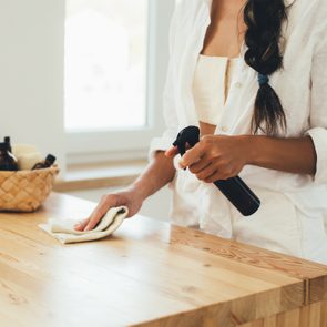 Young woman cleaning wooden table using spray and natural rag in a kitchen.