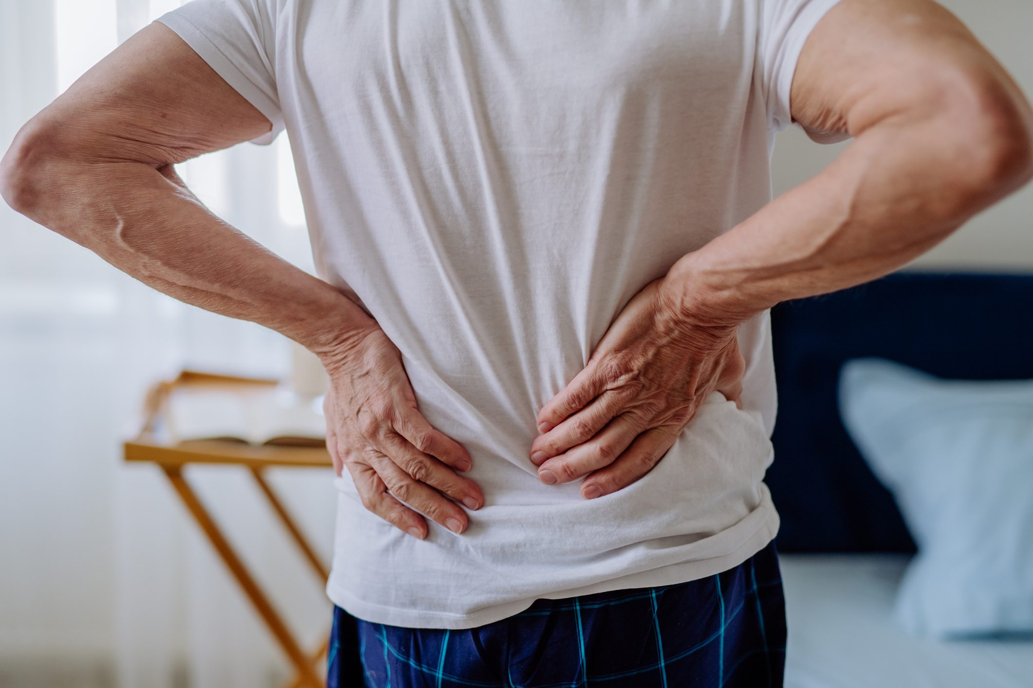 Senior man having back pain, standing in his bedroom.