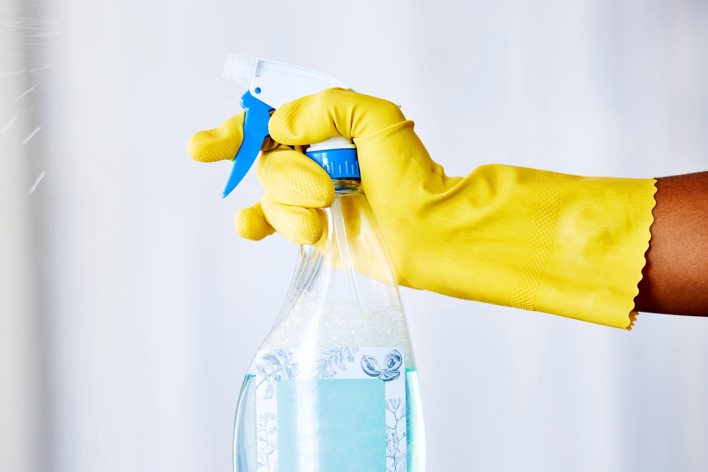 yellow glove hand holding spray cleaner pretreating stains in the bathroom