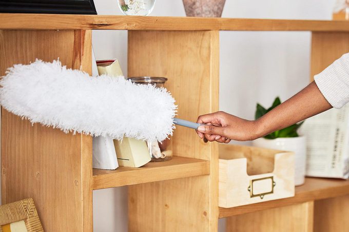 using a duster to dust a shelf