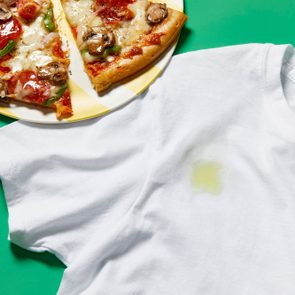 Oil and grease stain on white tshirt from pizza, shown nearby, on green background