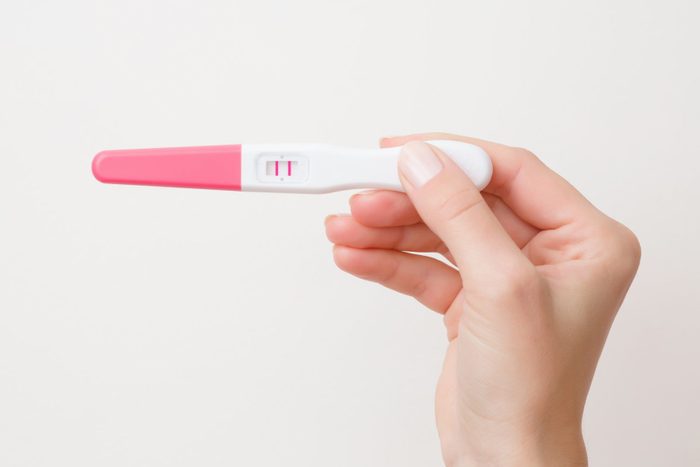Young woman's hand holding pregnancy test with two stripes on gray background. Positive result. Closeup. Point view shot. Empty place for text.