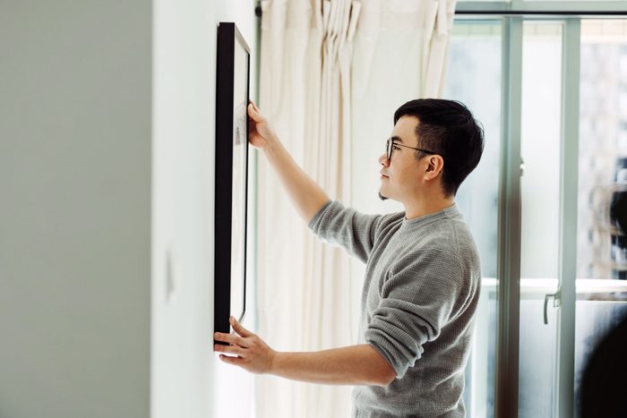 young man hanging a picture upside down to prank parents