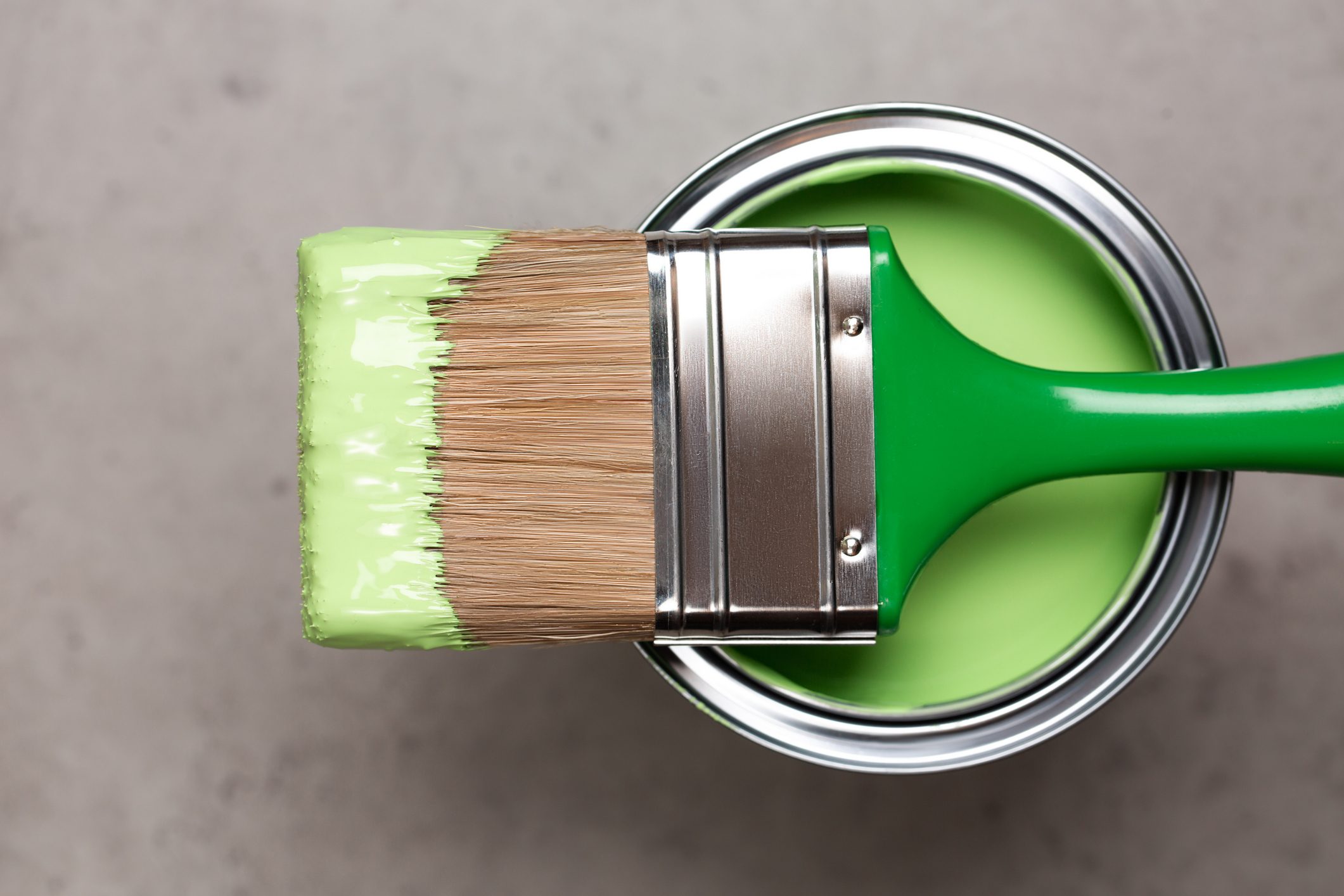 Paintbrush on metal bucket with green pigment for renovation works on concrete gray background. Redecoration concept in home interior. Flat lay style and close-up