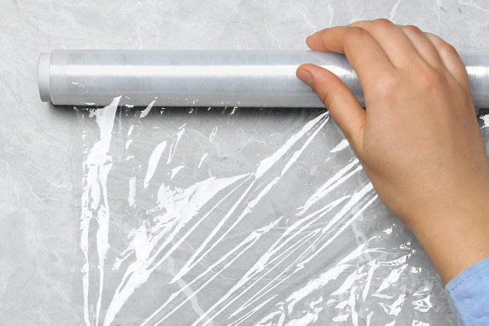 Woman with roll of stretch wrap at light grey table, top view