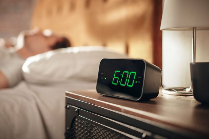 alarm clock that says 6am with sleeping man in background