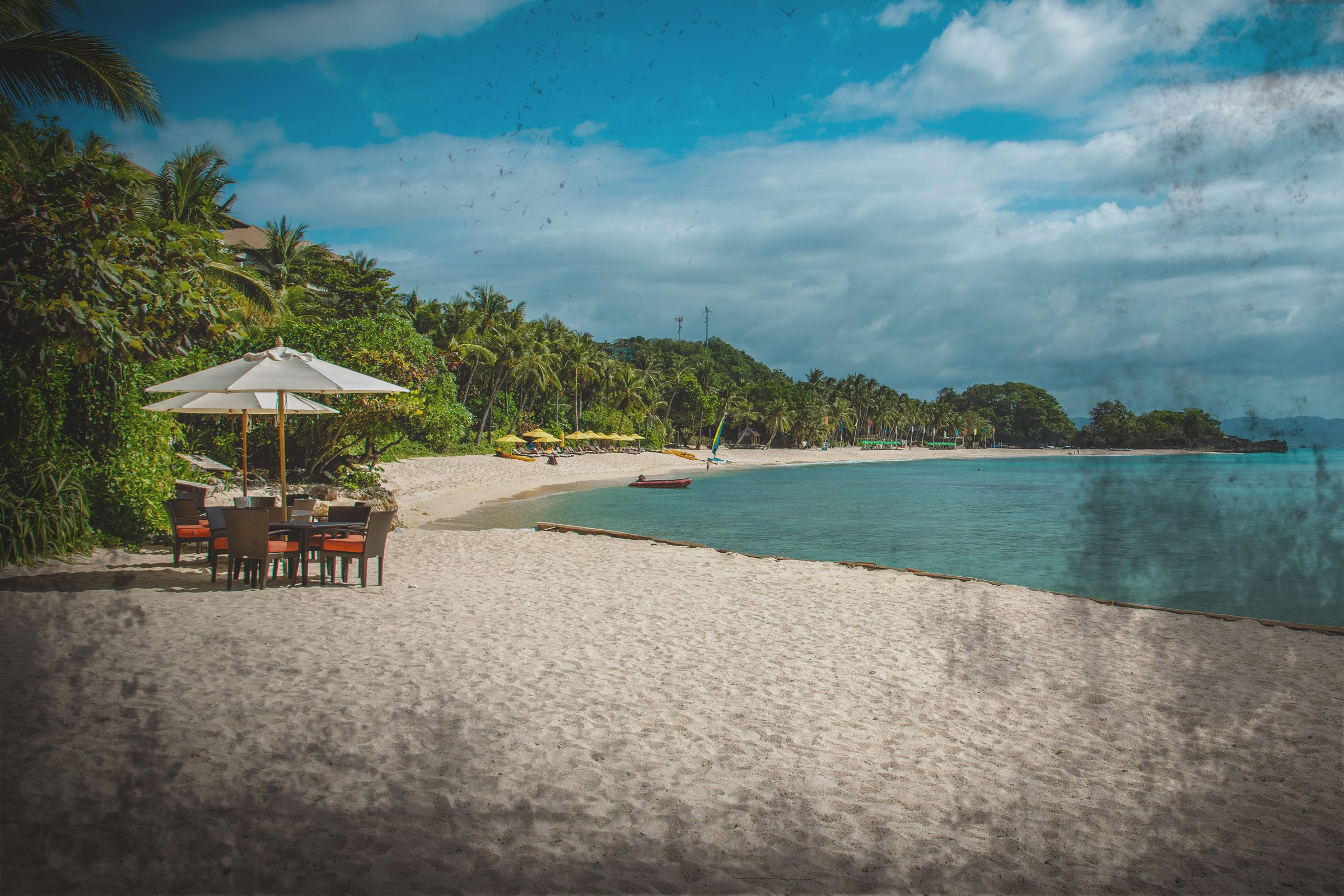 table and chairs on a desolate beach in the Philippines with a dark vignette on the image to represent danger