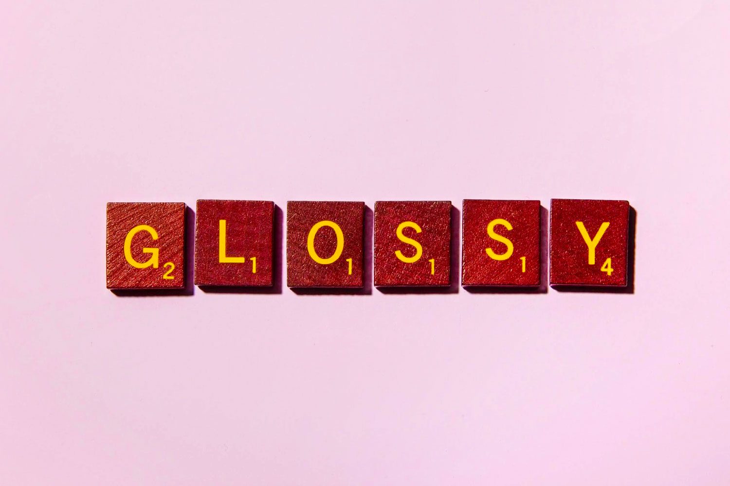 word GLOSSY in scrabble tiles on pink background