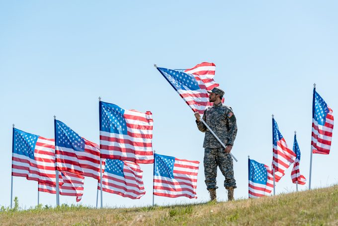 selective focus of handsome man in military uniform and cap standing and holding american flag
