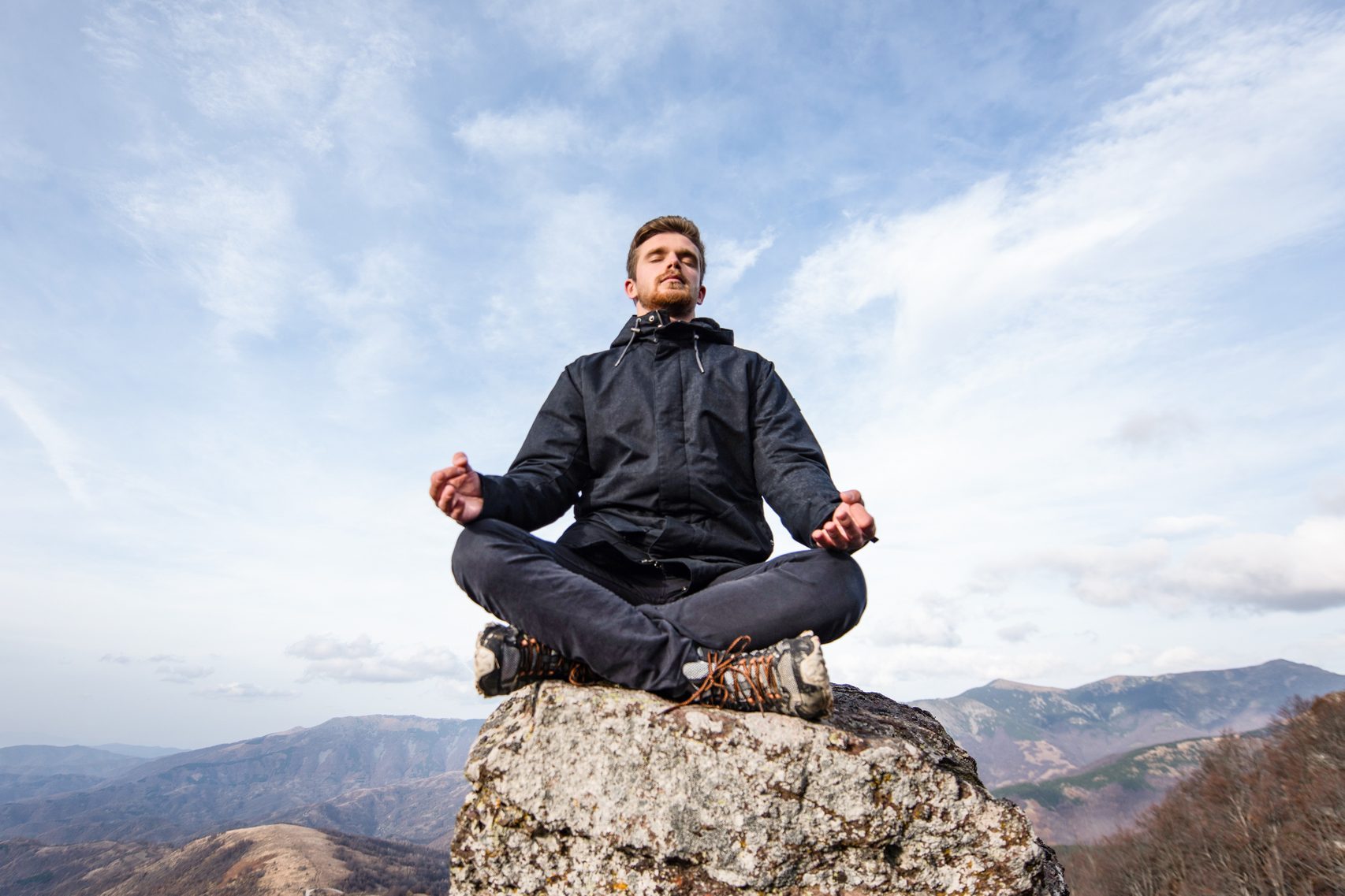 Young man meditating on mountain top.