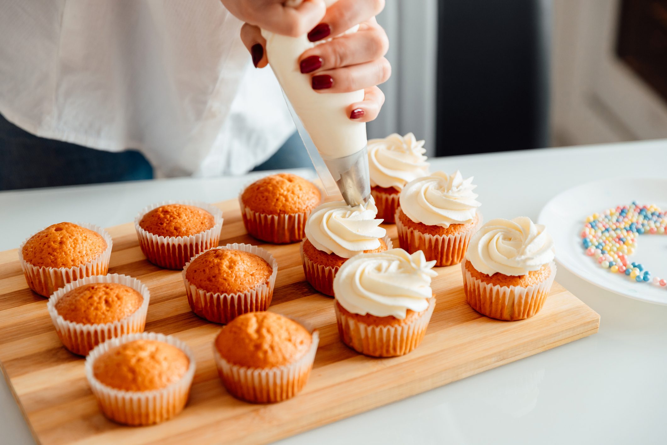 Woman decorates freshly baked cupcakes with cream