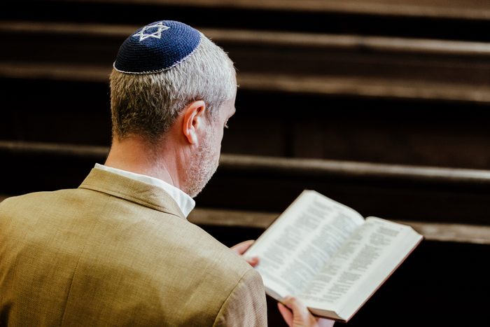 Jewish man wearing yarmulke while reading holy book in synagogue