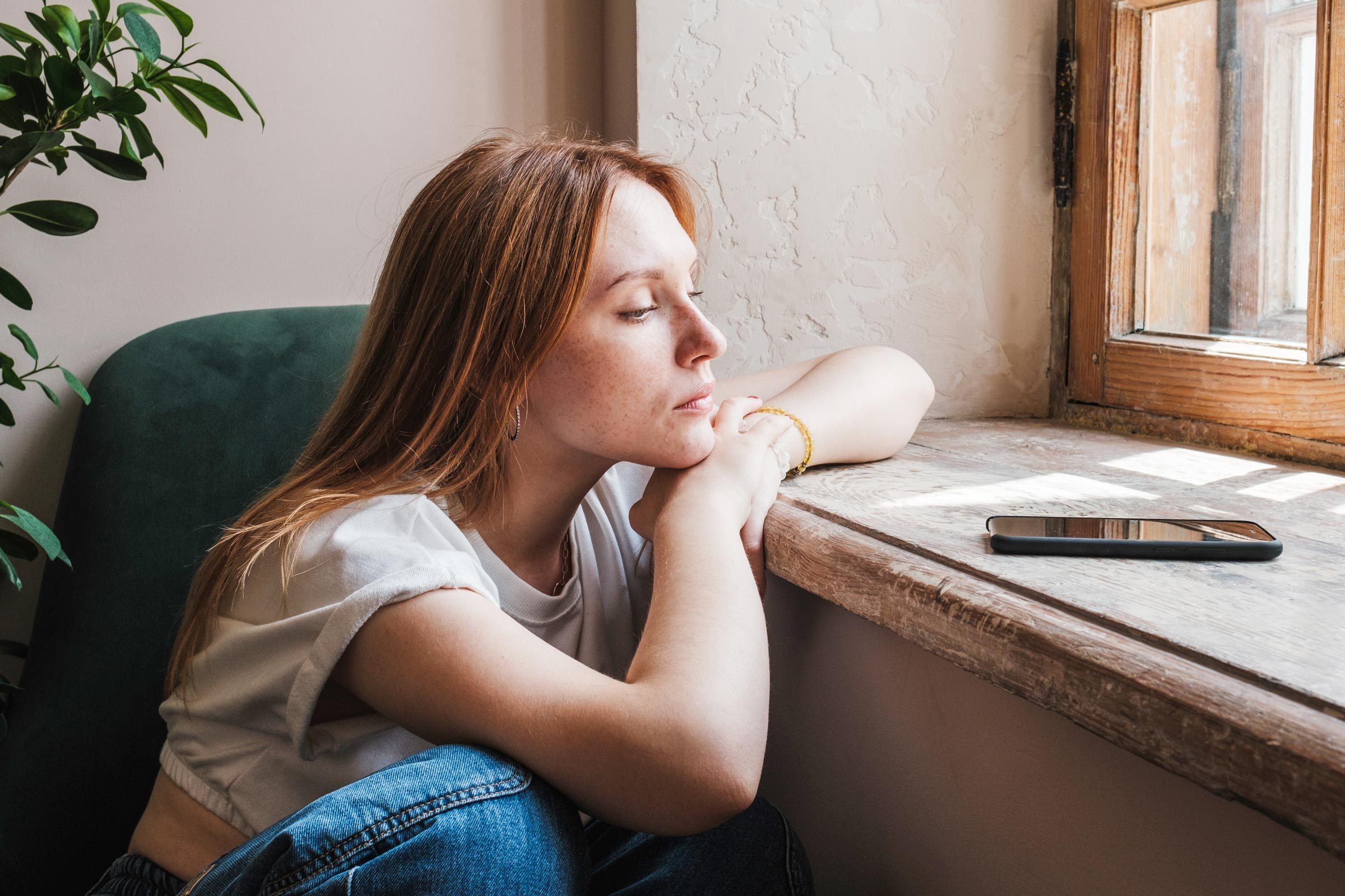 upset woman by a phone sitting by the window