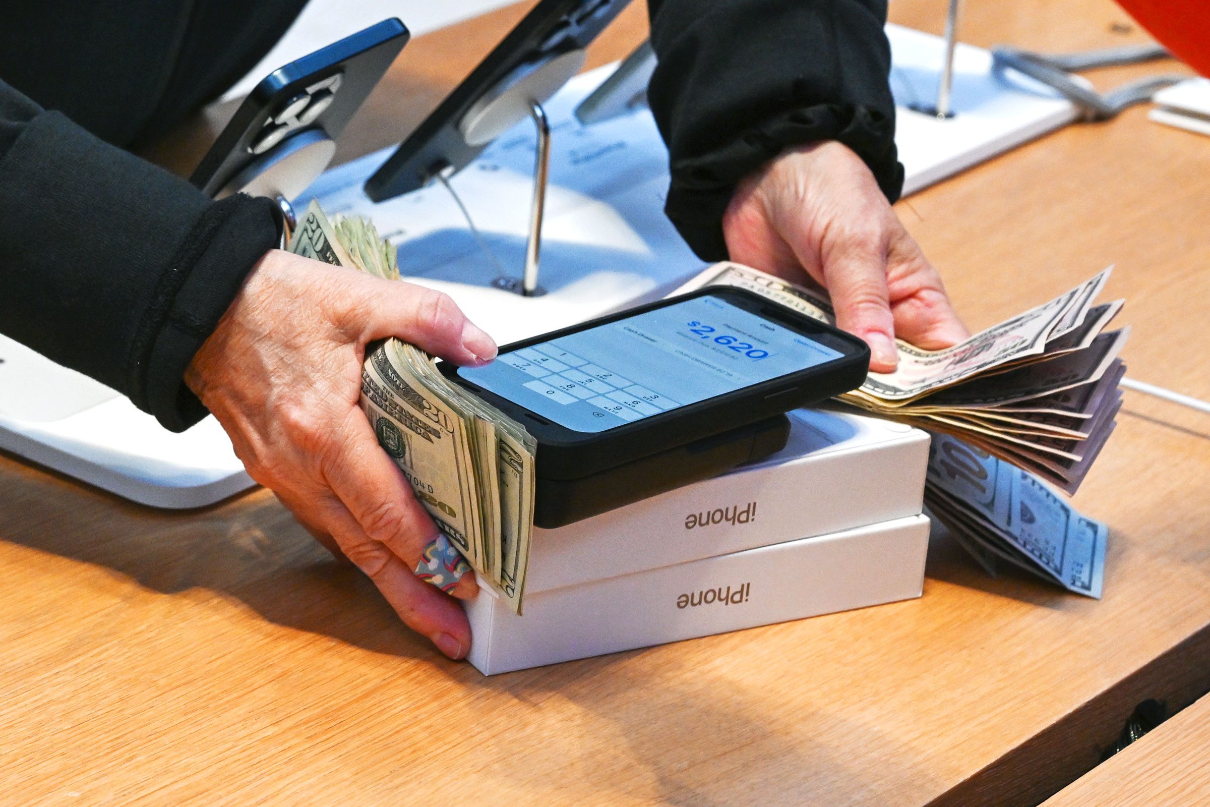 hands holding a lot of money and two iPhone boxes while checking out at the apple store