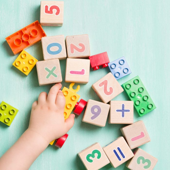 Child playing with wooden cubes with numbers and colorful toy bricks on a turquoise wooden background. Toddler learning numbers. Hand of a child taking toys.