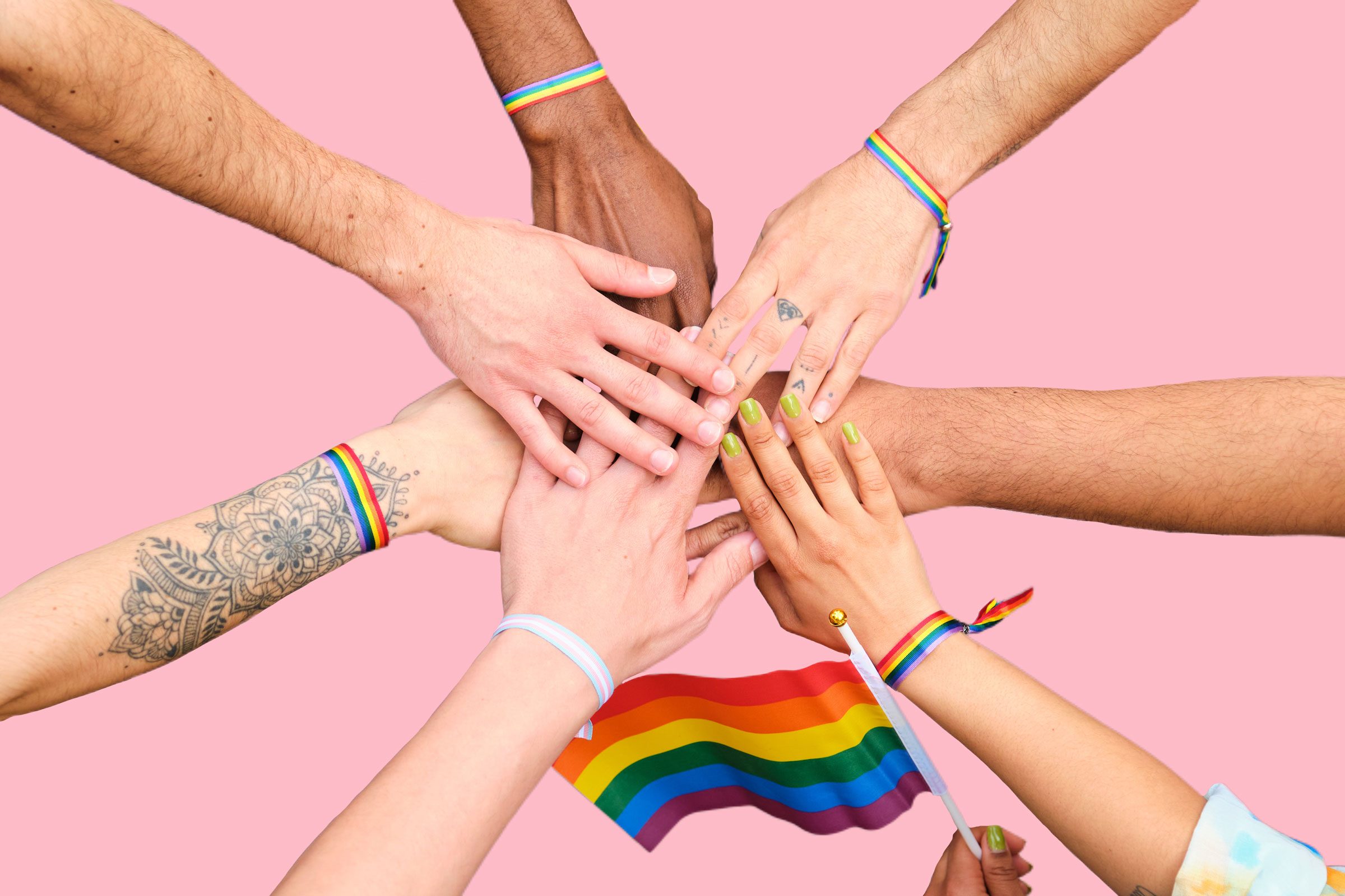 A group of people stacking hands and holding rainbow flags on a pink background
