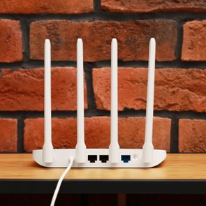 New white Wi-Fi router on wooden table near brick wall