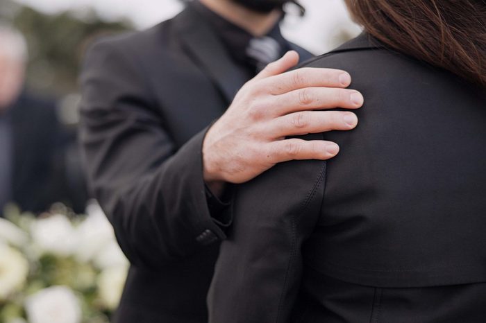 Funeral, support and people care for grief, mourning or depressed mother at burial ceremony, memorial service or cemetery. Hand, shoulder and man helping sad woman with love, advice or family comfort