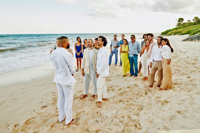 Extreme wide shot of gay couple getting married on tropical beach in front of friends and family