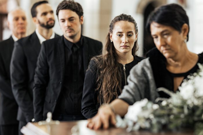 Funeral, goodbye and family with a coffin in a church during a service in death, mourning and grief. Respect, greeting and sad people in a row with a casket in a cathedral for a burial or memorial