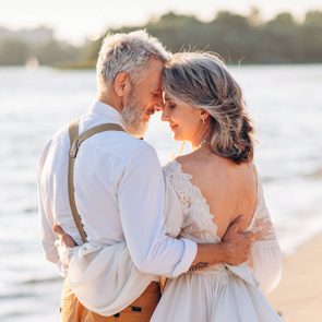 Stylish Couple Of Elderly Newlyweds Stand Embracing On River Bank