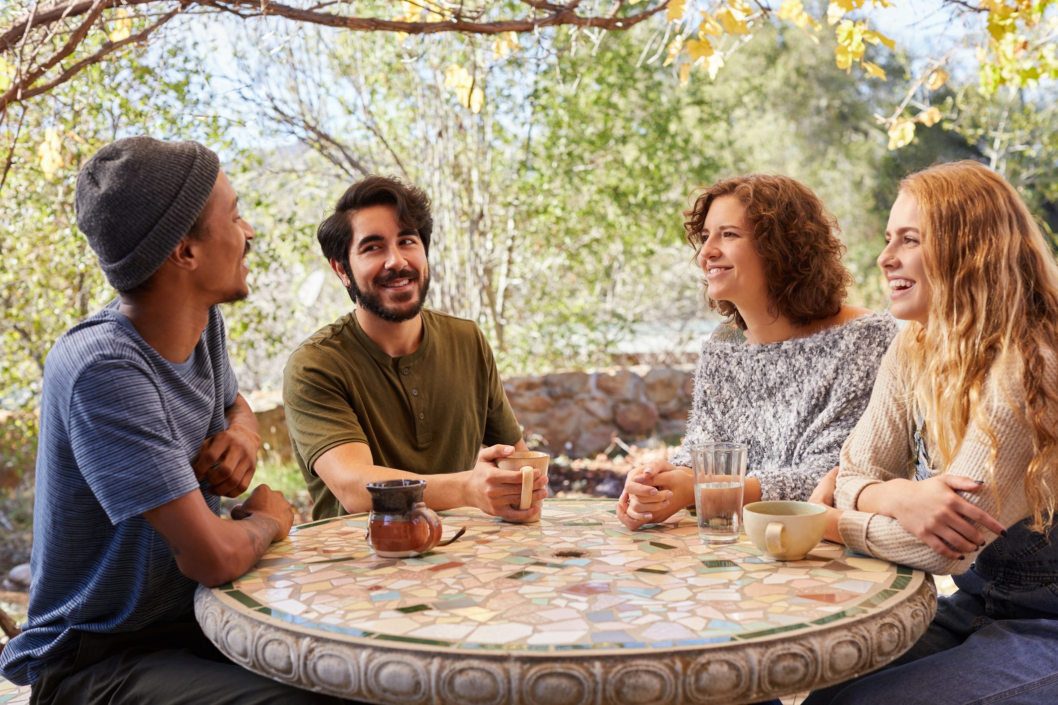 Smiling young friends having coffee around a table outside