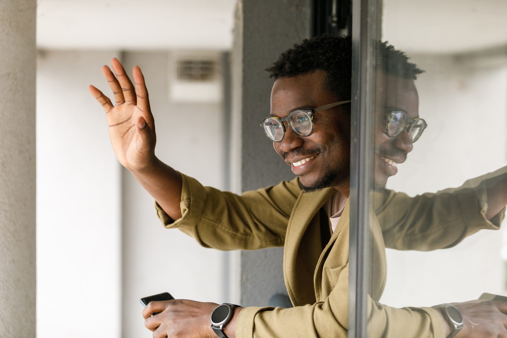 Businessman leaning against open window, waving at colleague coming to work