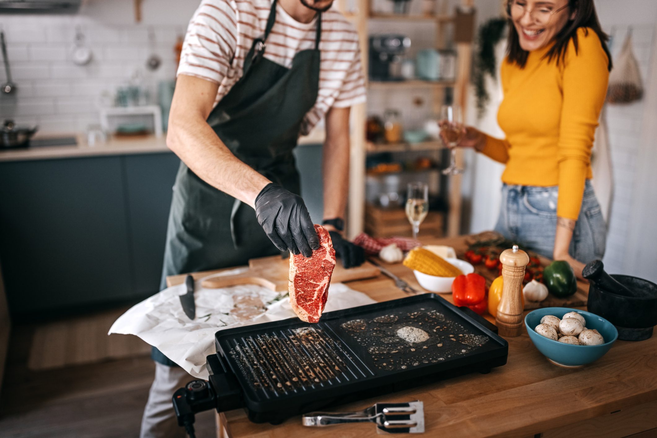 Woman standing with friend preparing steak in kitchen at home