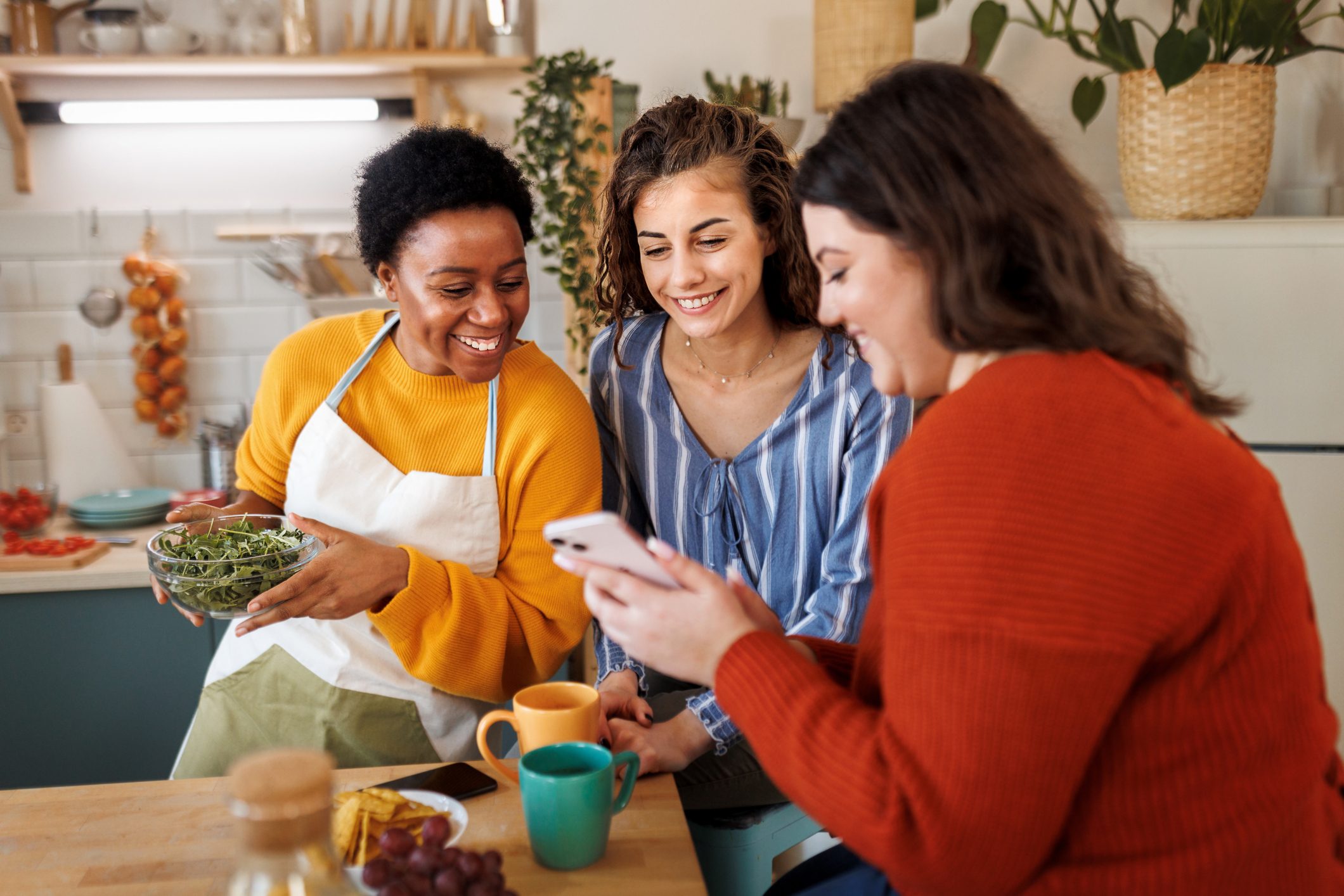 Young smiling female friends using phone in the kitchen