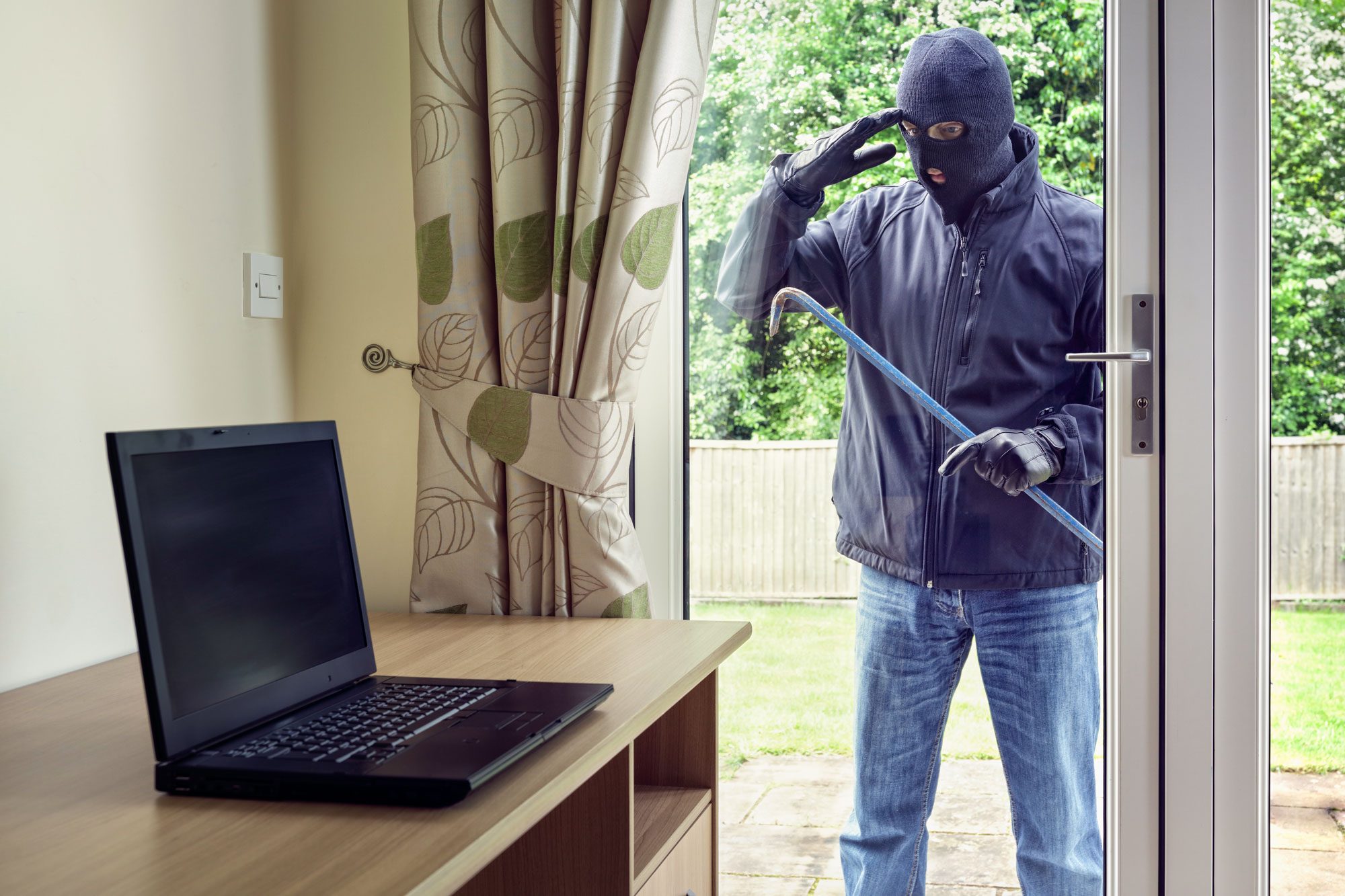 Thief Looking Through Patio Doors Window At A Laptop Computer To Steal