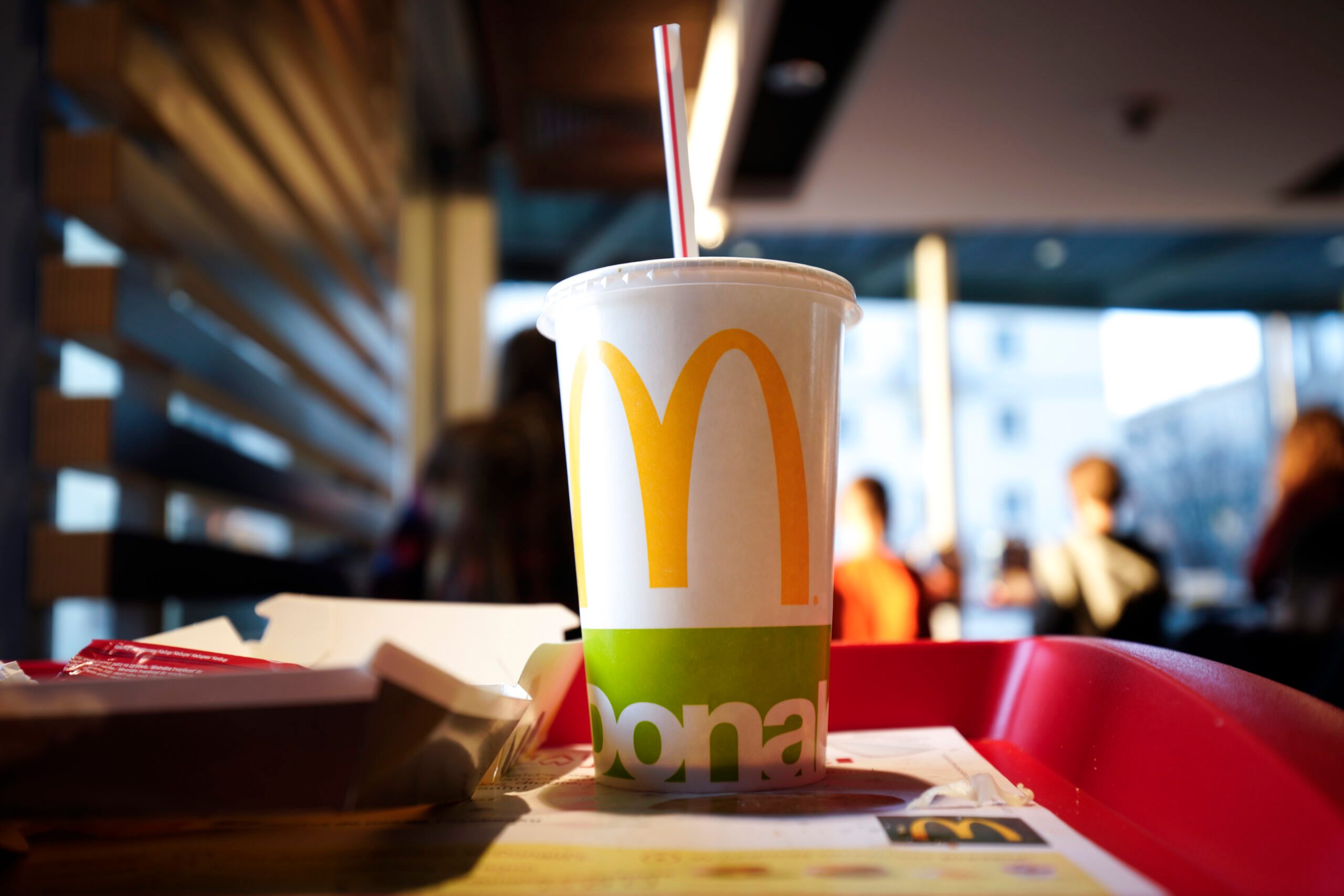 a dramatically lit, low angle of a mcdonalds cup on a tray in a mcdonalds restaurant. Other customers out of focus in the background