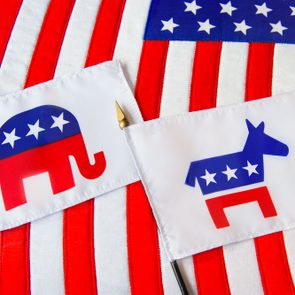 Republican Elephant And Democratic Donkey Political Party Symbols On Two Small Flags Laying On The American Flag