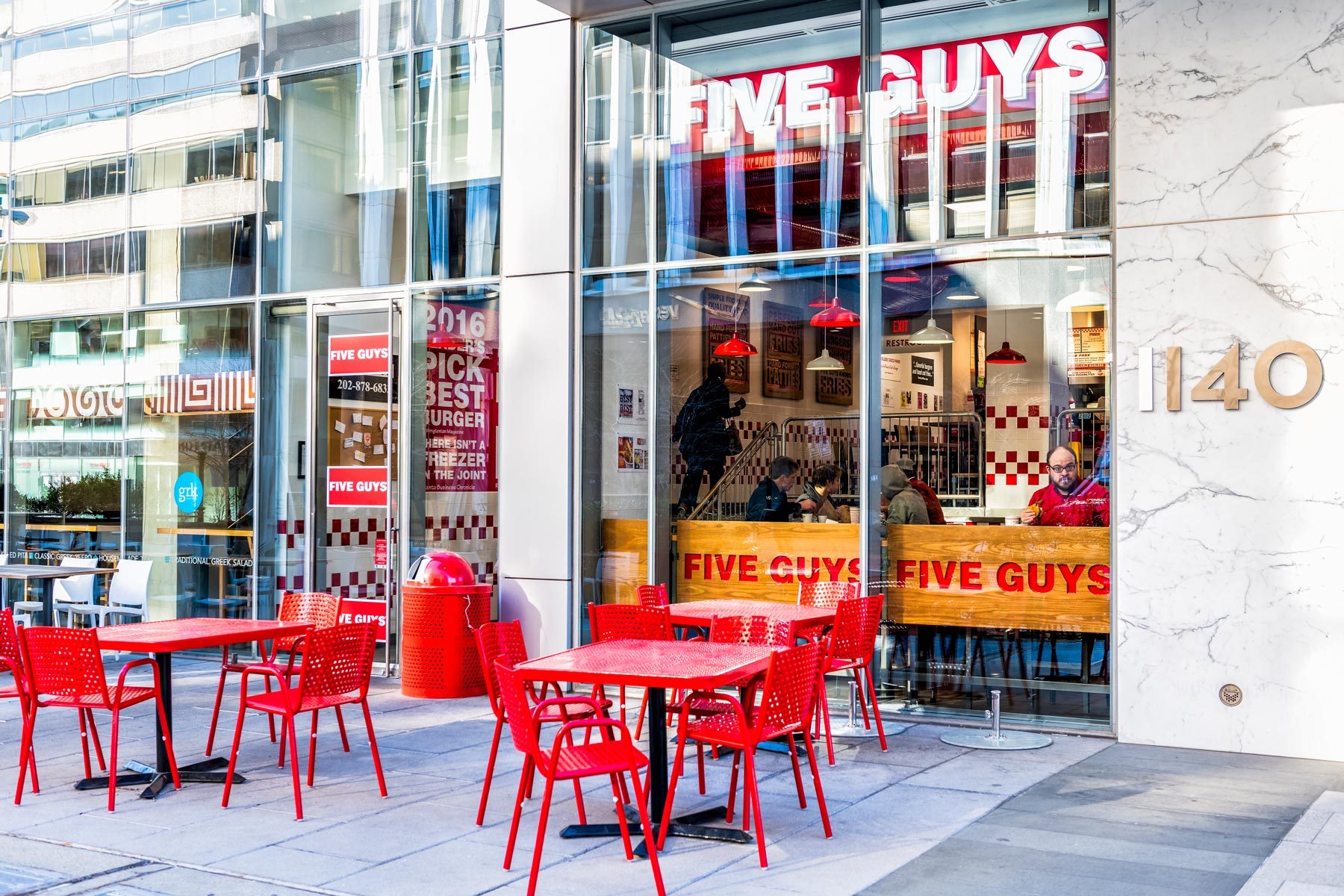 Five Guys restaurant, store burger chain entrance in District of Columbia with chairs, tables, outside, outdoor sitting area, people inside eating