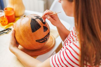 Woman Painting Face On Pumpkin For Halloween