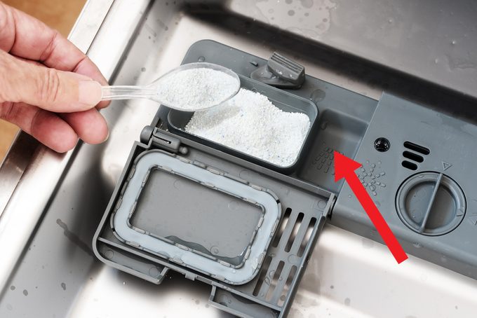 Hand is pouring white washing powder into a dishwasher