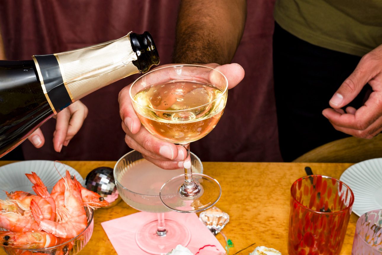 Hand Pouring Champagne For Friend At New Year's Eve Party