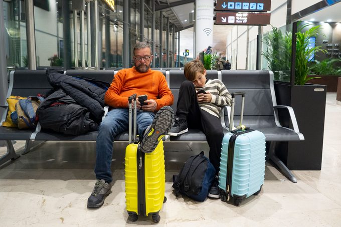 Father And Son Waiting For Flight At The Airport Lounge
