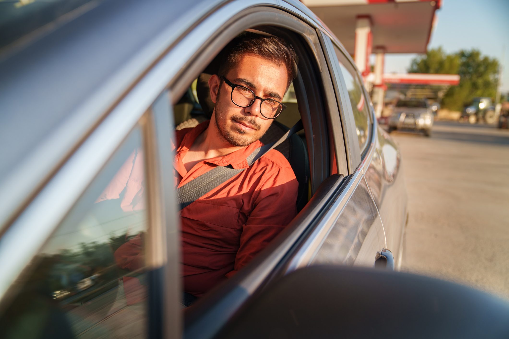 Man is at the gas station in the car looking in his side view mirror