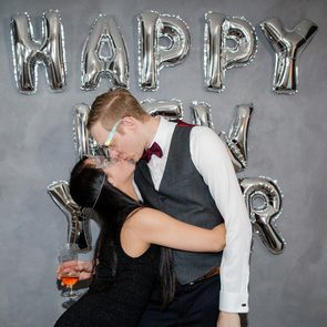 A Young Couple Kiss in Front of a Happy New Year Sign in their Home in Oslo, Norway