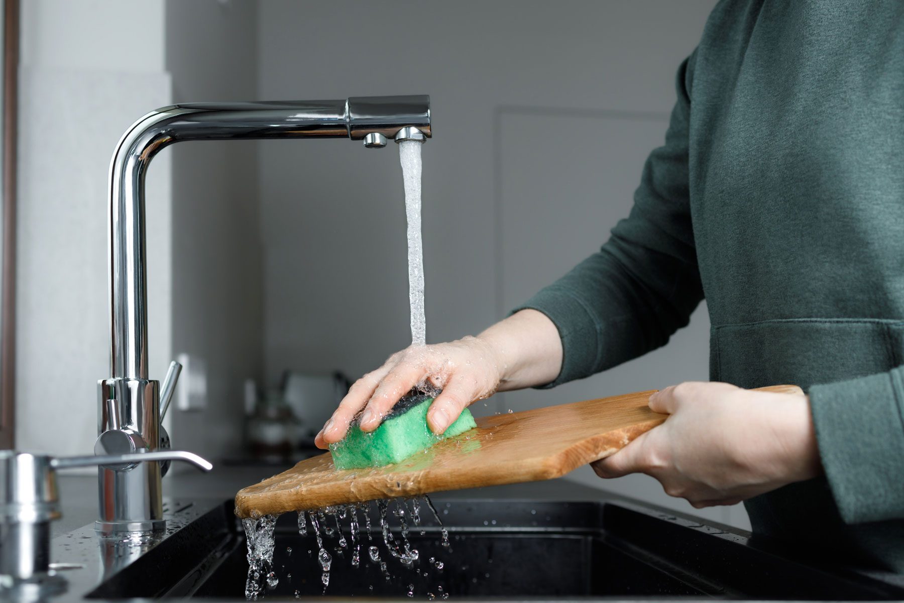 woman washing wooden cutting board under water stream in sink