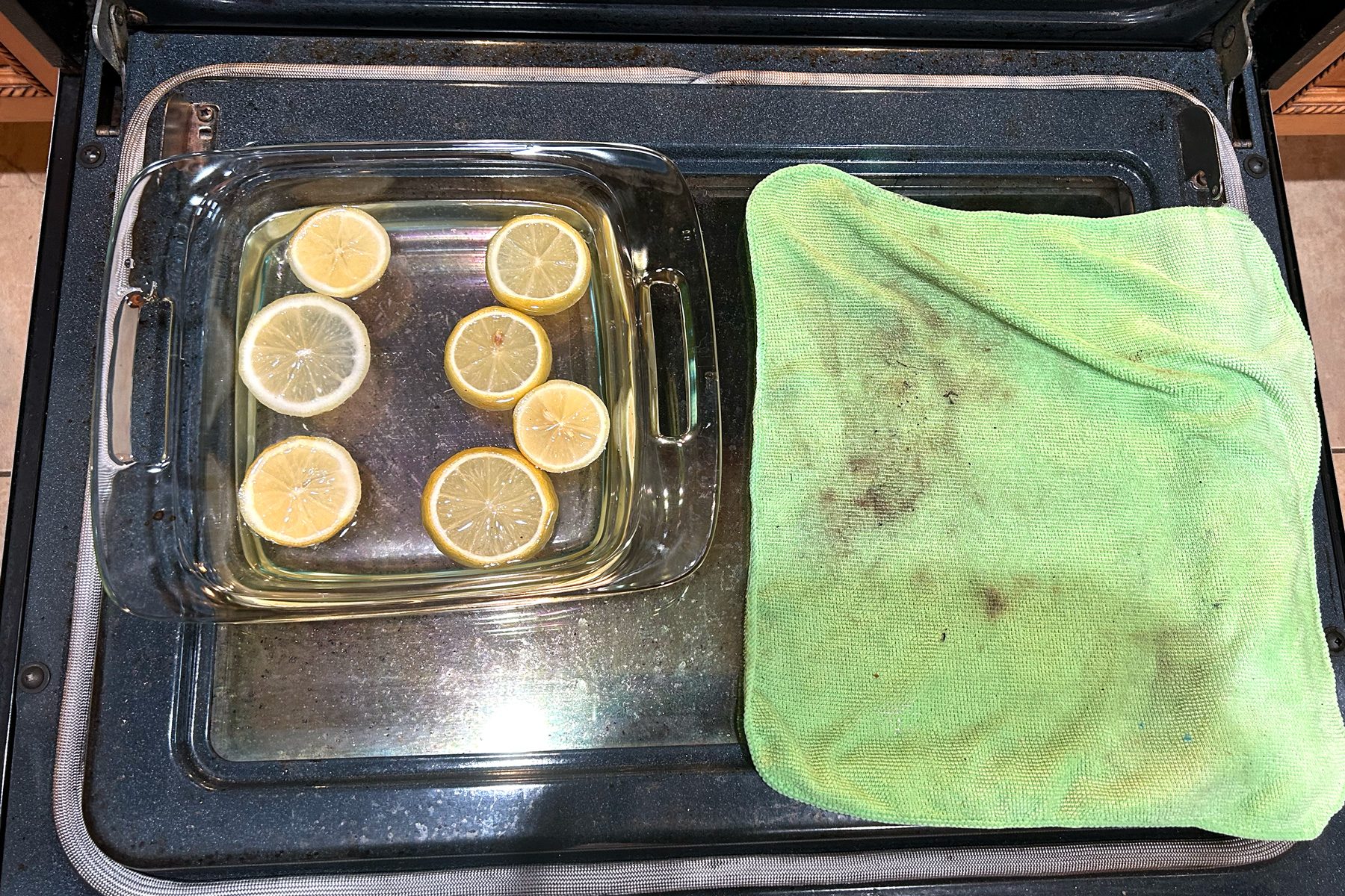 A clear glass pan containing several ripe lemons with a green color microfiber cloth