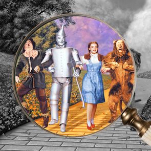 Actors Ray Bolger, Jack Haley, Judy Garland and Bert Lahr in costume on the yellow brick road in a scene from the film 'The Wizard of Oz', 1939, with an overlay of a magnifying glass. Inside the lens of the magnifying glass, the image is in color, outside the lens the image is in black and white.