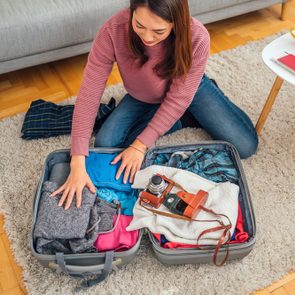 Young Cheerful Japanese Woman Packing A Suitcase