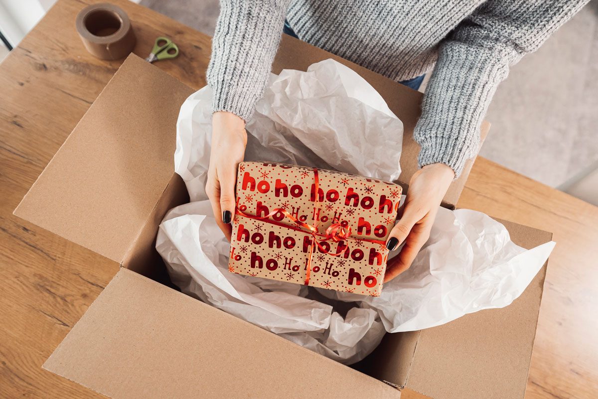 Woman Hands Holding A Christmas Present Putting It Inside A Cardboard Box