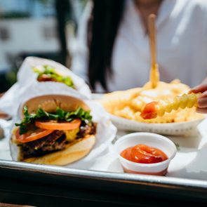 Person dipping fries in ketchup alongside a burger