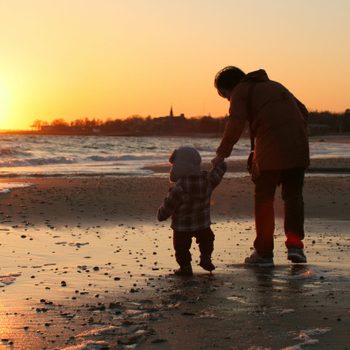 Mother and baby walking on the beach wearing coats and pants at sunset