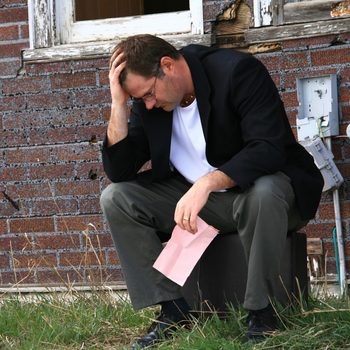 Distressed man holding Pink Slip with head in hand on the grass outside a brick building