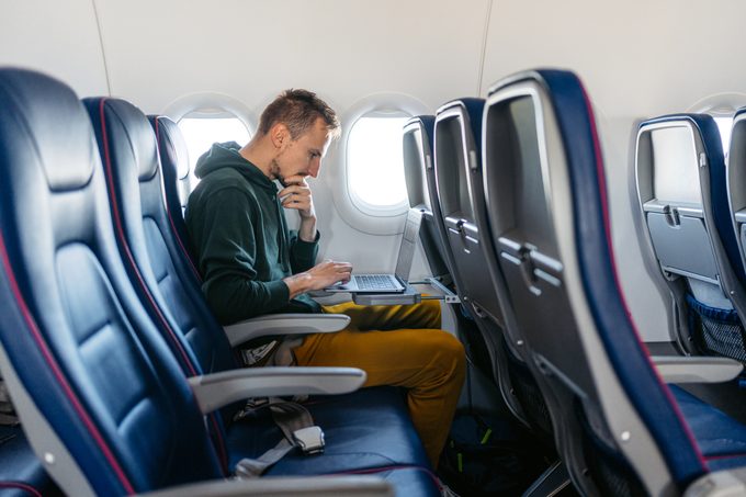 Man using a laptop in an airplane seat